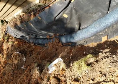 Foundation repair project showing exposed soil, drainage pipe, and protective barrier, illustrating Southern Structural Solutions' work in structural solutions for residential properties.