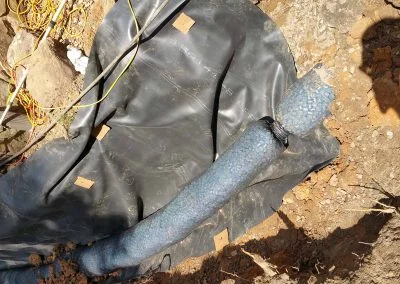 Foundation repair materials including black plastic sheeting and a blue drainage pipe, showcasing Southern Structural Solutions' work on residential properties.