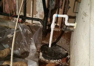 Sump pump installation in a crawl space with exposed pipes and gravel, showcasing foundation repair work by Southern Structural Solutions.