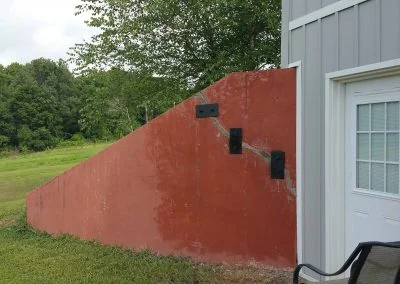 Foundation repair work on a residential property showcasing a sloped red wall with visible structural supports, surrounded by greenery.