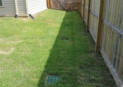 Lawn area with drainage system and wooden fence, showcasing foundation repair work by Southern Structural Solutions.